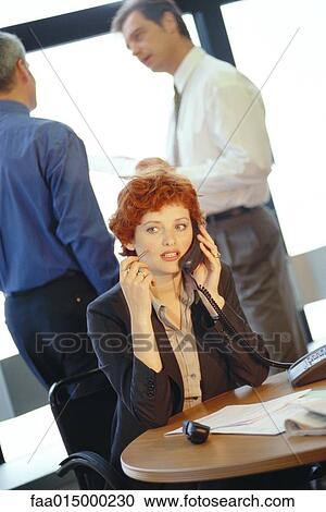 Businesswoman sitting at table using phone, colleagues in background View Large Photo Image Stock Image - Businesswoman sitting at table using phone, colleagues in background. Fotosearch