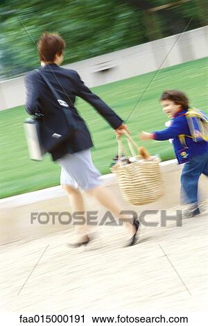 Stock Image - Businesswoman walking with son, blurred motion. Fotosearch