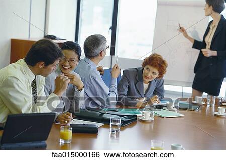 Stock Photograph - Colleagues at table talking to each other, laughing, during business presentation. Fotosearch