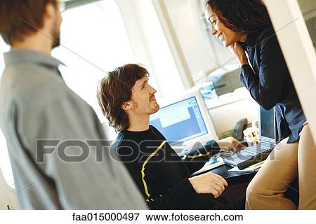 Colleagues in office, woman sitting on edge of desk facing man View Large Photo Image Stock Photo - Colleagues in office, woman sitting on edge of desk facing man. Fotosearch