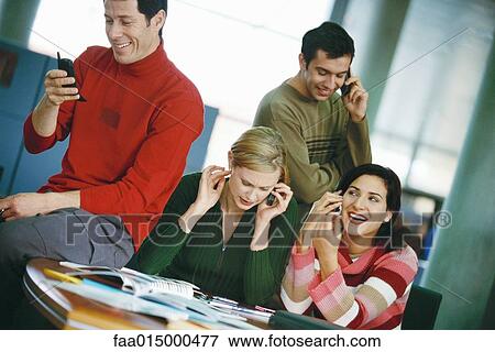 Colleagues sitting around table, using cell phones View Large Photo Image Stock Photo - Colleagues sitting around table, using cell phones. Fotosearch