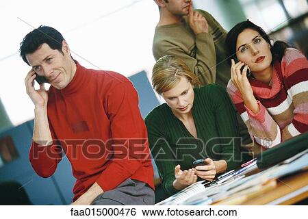 Colleagues sitting around table, using cell phones View Large Photo Image Stock Photograph - Colleagues sitting around table, using cell phones. Fotosearch