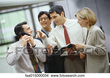 Picture - Four business colleagues standing in a group, one using phone, others listening. Fotosearch