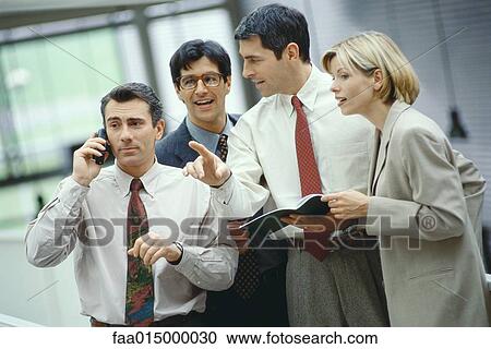 Four business colleagues standing in a group, one using phone, others listening View Large Photo Image Stock Image - Four business colleagues standing in a group, one using phone, others listening. Fotosearch