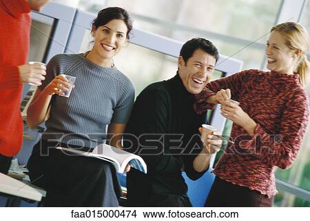 Picture - Four colleagues, holding cups of coffee and water, laughing. Fotosearch