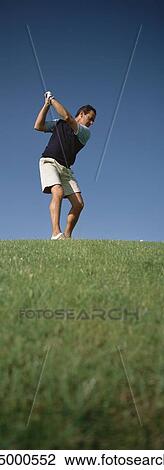 Stock Image - Golfer swinging, low angle view. Fotosearch