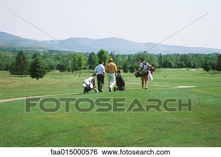 Stock Photograph - Golfers walking across golf course, rear view. Fotosearch
