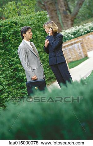 Male and female business associates standing outoors, woman using phone View Large Photo Image Stock Photo - Male and female business associates standing outoors, woman using phone. Fotosearch