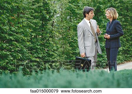 Male and female business associates standing outoors, woman using phone View Large Photo Image Stock Photo - Male and female business associates standing outoors, woman using phone. Fotosearch