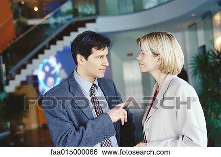 Male and female business associates standing in lobby, man pointing at woman View Large Photo Image Stock Photograph - Male and female business associates standing in lobby, man pointing at woman. Fotosearch