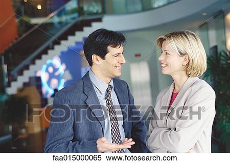 Male and female business associates standing in lobby, talking and smiling View Large Photo Image Stock Photography - Male and female business associates standing in lobby, talking and smiling. Fotosearch