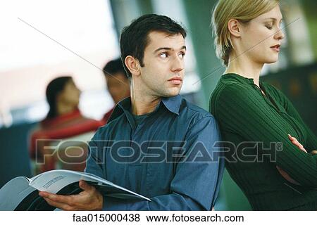 Man holding brochure, looking over shoulder at female colleague turning her back to him View Large Photo Image Stock Photo - Man holding brochure, looking over shoulder at female colleague turning her back to him. Fotosearch