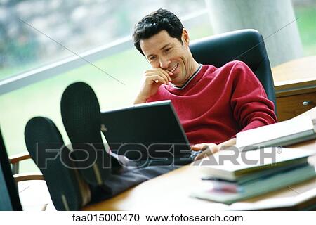 Man sitting at desk with feet up, using laptop View Large Photo Image Stock Image - Man sitting at desk with feet up, using laptop. Fotosearch