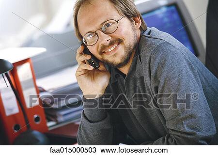 Man using cell phone in office, smiling View Large Photo Image Stock Image - Man using cell phone in office, smiling. Fotosearch