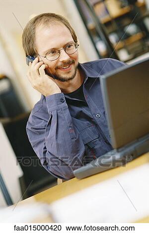Stock Image - Man using laptop and cell phone. Fotosearch