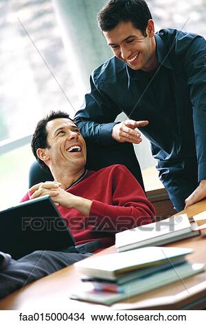 Man using laptop, looking at second man looking over shoulder, laughing View Large Photo Image Picture - Man using laptop, looking at second man looking over shoulder, laughing. Fotosearch