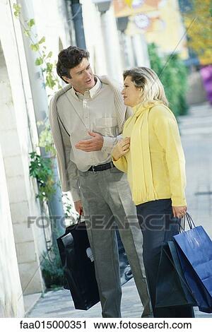 Mature couple standing on sidewalk, holding shopping bags and talking View Large Photo Image Stock Image - Mature couple standing on sidewalk, holding shopping bags and talking. Fotosearch