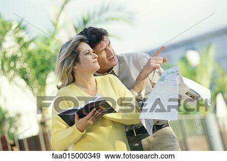 Mature couple standing outdoors with map and guidebook, man pointing View Large Photo Image Stock Photo - Mature couple standing outdoors with map and guidebook, man pointing. Fotosearch