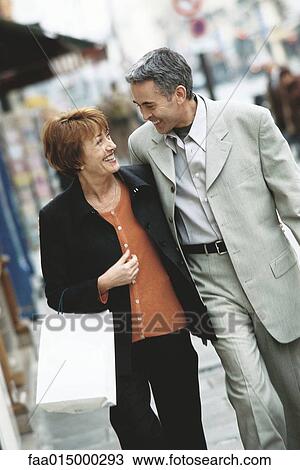 Mature couple walking on city sidewalk, smiling at each other View Large Photo Image Stock Image - Mature couple walking on city sidewalk, smiling at each other. Fotosearch