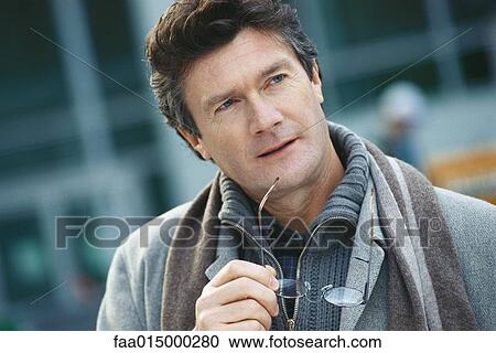 Mature man holding glasses to chin, looking away View Large Photo Image Stock Image - Mature man holding glasses to chin, looking away. Fotosearch