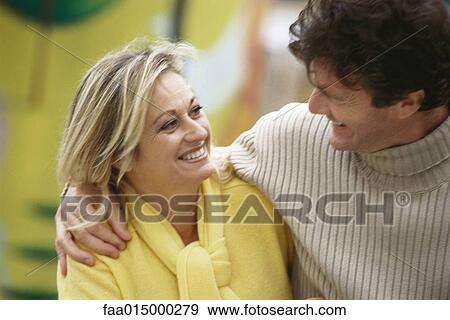 Middle aged couple smiling at each other, man's arm around woman's shoulders View Large Photo Image Stock Photo - Middle aged couple smiling at each other, man's arm around woman's shoulders. Fotosearch