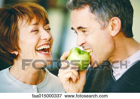 Senior man eating apple, senior woman laughing, close-up View Large Photo Image Stock Photo - Senior man eating apple, senior woman laughing, close-up. Fotosearch