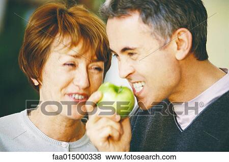 Senior man eating apple, senior woman laughing, close-up View Large Photo Image Stock Photo - Senior man eating apple, senior woman laughing, close-up. Fotosearch