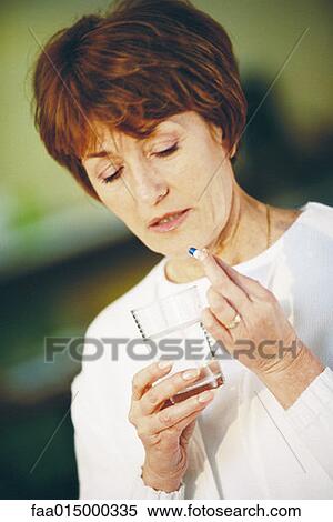 Stock Photography - Senior woman taking pill, holding glass of water. Fotosearch