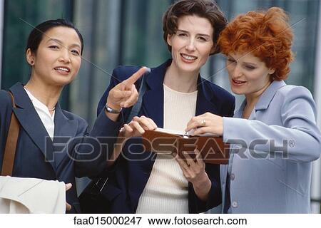 Three businesswoman looking at agenda, one pointing out of frame View Large Photo Image Stock Photo - Three businesswoman looking at agenda, one pointing out of frame. Fotosearch
