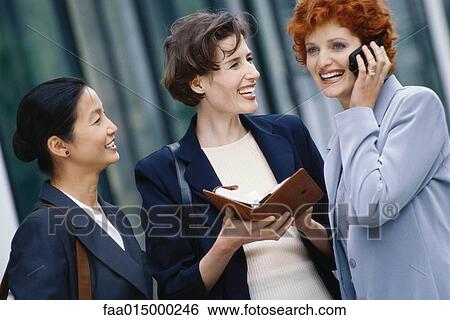 Stock Photograph - Three businesswoman, one holding agenda, one using cell phone. Fotosearch