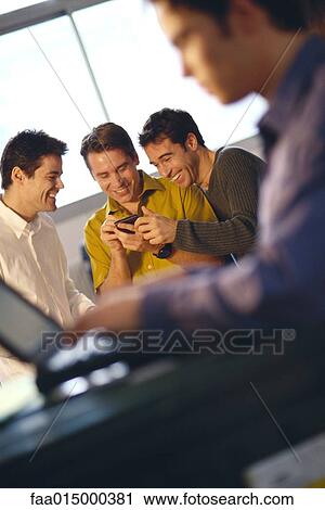 Stock Image - Three young men using electronic organizer, laptop user in foreground. Fotosearch