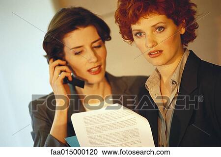 Two business women, holding document while one uses cell phone View Large Photo Image Stock Image - Two business women, holding document while one uses cell phone. Fotosearch