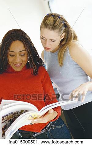Stock Image - Two female colleagues looking at catalog together. Fotosearch