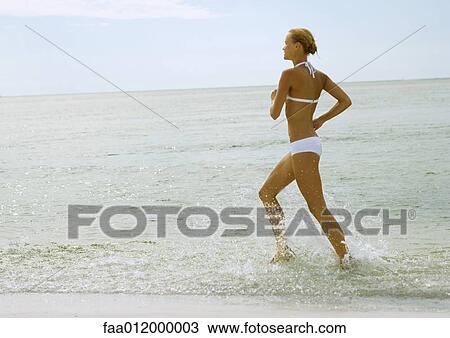 Stock Image - Woman in bikini running in surf at beach. Fotosearch