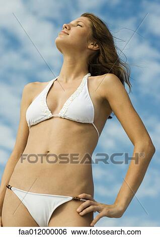 Woman in bikini standing with hand on hip, sky in background, low angle view View Large Photo Image Stock Photograph - Woman in bikini standing with hand on hip, sky in background, low angle view. Fotosearch