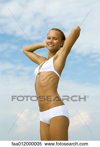 Stock Photography - Woman in bikini stretching with hands behind head, low angle view. Fotosearch