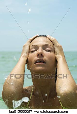 Stock Photo - Woman in sea, hands on head and eyes closed, close-up. Fotosearch