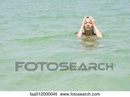 Stock Photography - Woman in sea, hands on head. Fotosearch