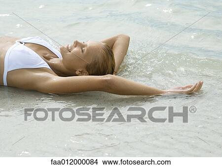 Woman lying in shallow water on beach, smiling with eyes closed View Large Photo Image Picture - Woman lying in shallow water on beach, smiling with eyes closed. Fotosearch