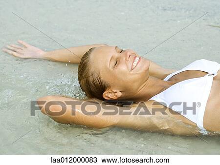 Woman lying in shallow water on beach, smiling with eyes closed View Large Photo Image Stock Image - Woman lying in shallow water on beach, smiling with eyes closed. Fotosearch