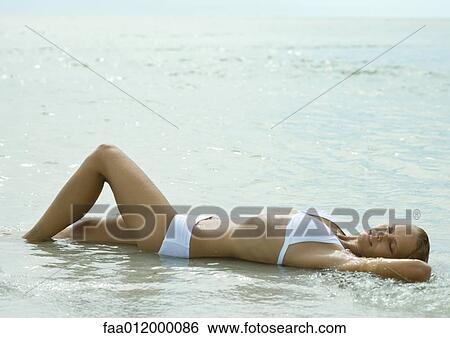 Woman lying in shallow water on beach, full length View Large Photo Image Stock Photograph - Woman lying in shallow water on beach, full length. Fotosearch