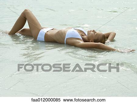 Woman lying in shallow water on beach, full length View Large Photo Image Stock Photography - Woman lying in shallow water on beach, full length. Fotosearch