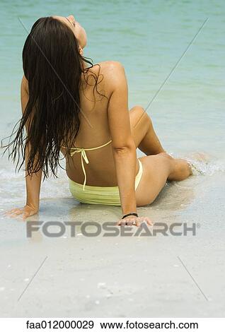 Woman sitting on sand with feet in surf, leaning back, rear view View Large Photo Image Stock Photo - Woman sitting on sand with feet in surf, leaning back, rear view. Fotosearch