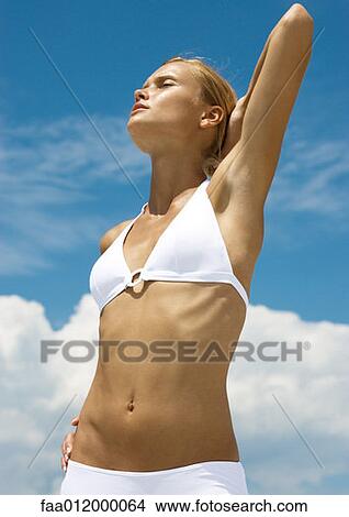 Woman wearing bikini, stretching with hand behind head, sky in background View Large Photo Image Picture - Woman wearing bikini, stretching with hand behind head, sky in background. Fotosearch
