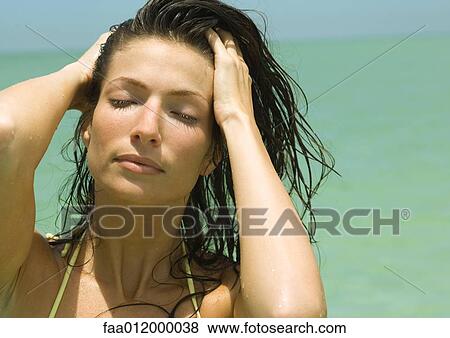 Stock Photo - Woman with hands in wet hair, sea in background, portrait. Fotosearch