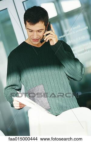 Young male office worker holding document, using telephone View Large Photo Image Picture - Young male office worker holding document, using telephone. Fotosearch