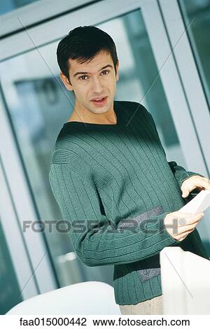 Stock Image - Young male office worker holding document, looking at camera. Fotosearch
