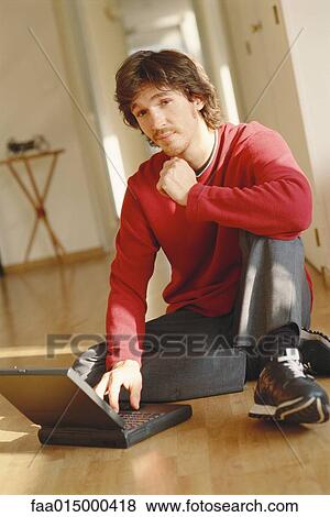 Young man sitting on floor, using laptop View Large Photo Image Stock Photo - Young man sitting on floor, using laptop. Fotosearch