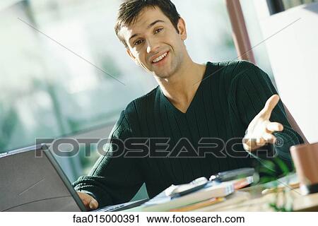 Young man using laptop, gesturing toward camera View Large Photo Image Stock Image - Young man using laptop, gesturing toward camera. Fotosearch