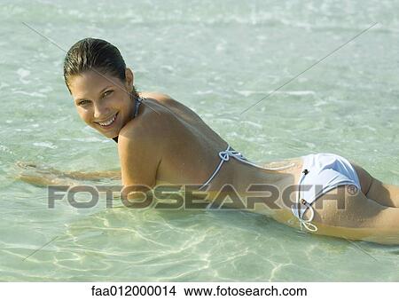 Young woman in bikini lying in shallow water on beach View Large Photo Image Picture - Young woman in bikini lying in shallow water on beach. Fotosearch